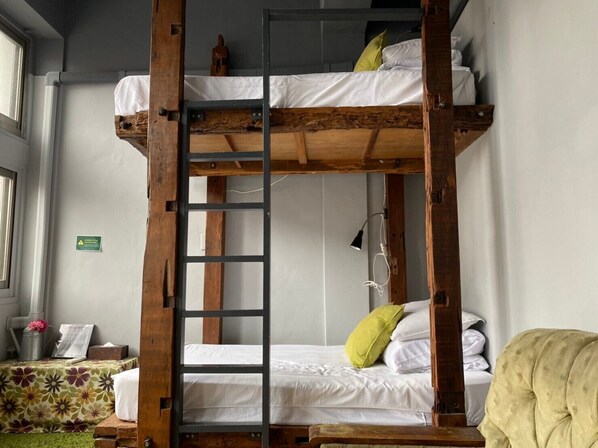 Una cama litera con escalera, ropa de cama blanca y una almohada verde.