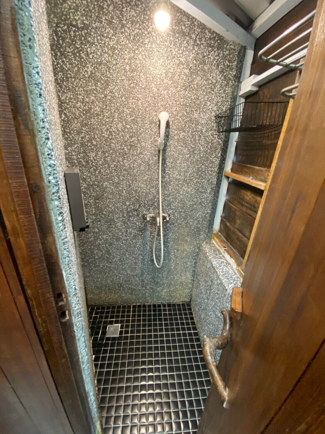 A shower with a textured wall, a metal grid floor, and a wooden door.