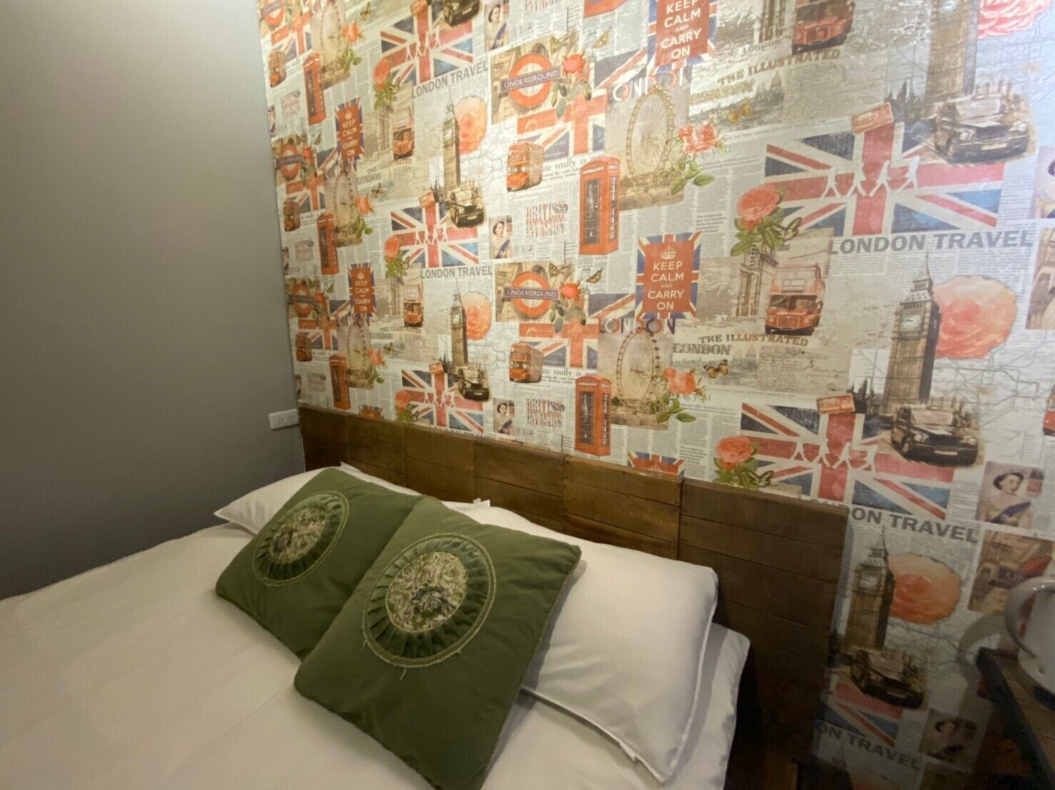 A hotel room with a bed, green pillows, and a wall decorated with London travel posters.