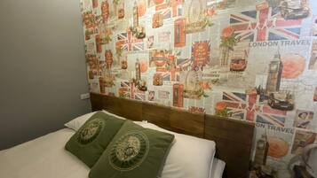 A hotel room with a bed, green pillows, and a wall decorated with London travel posters.