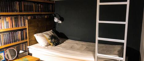 A compact room with a bunk bed, a bookshelf filled with books, and a small table with a mirror and a decorative item.