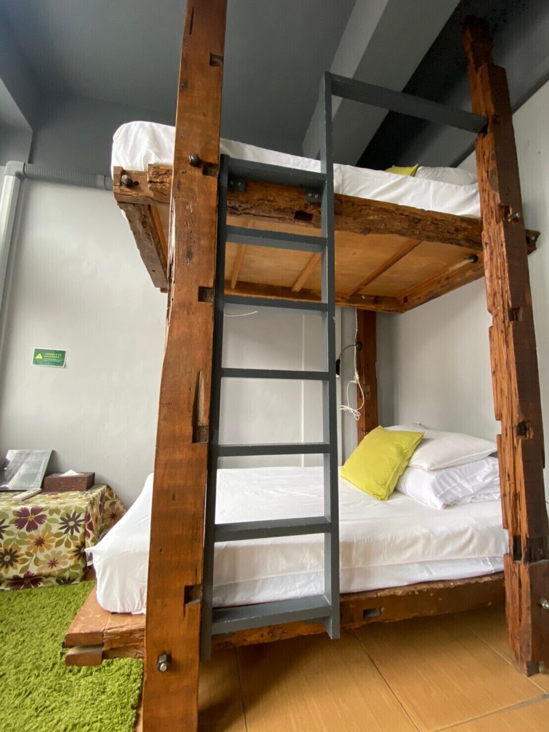A bunk bed with a wooden ladder, a green mat, and a floral-patterned cushion.