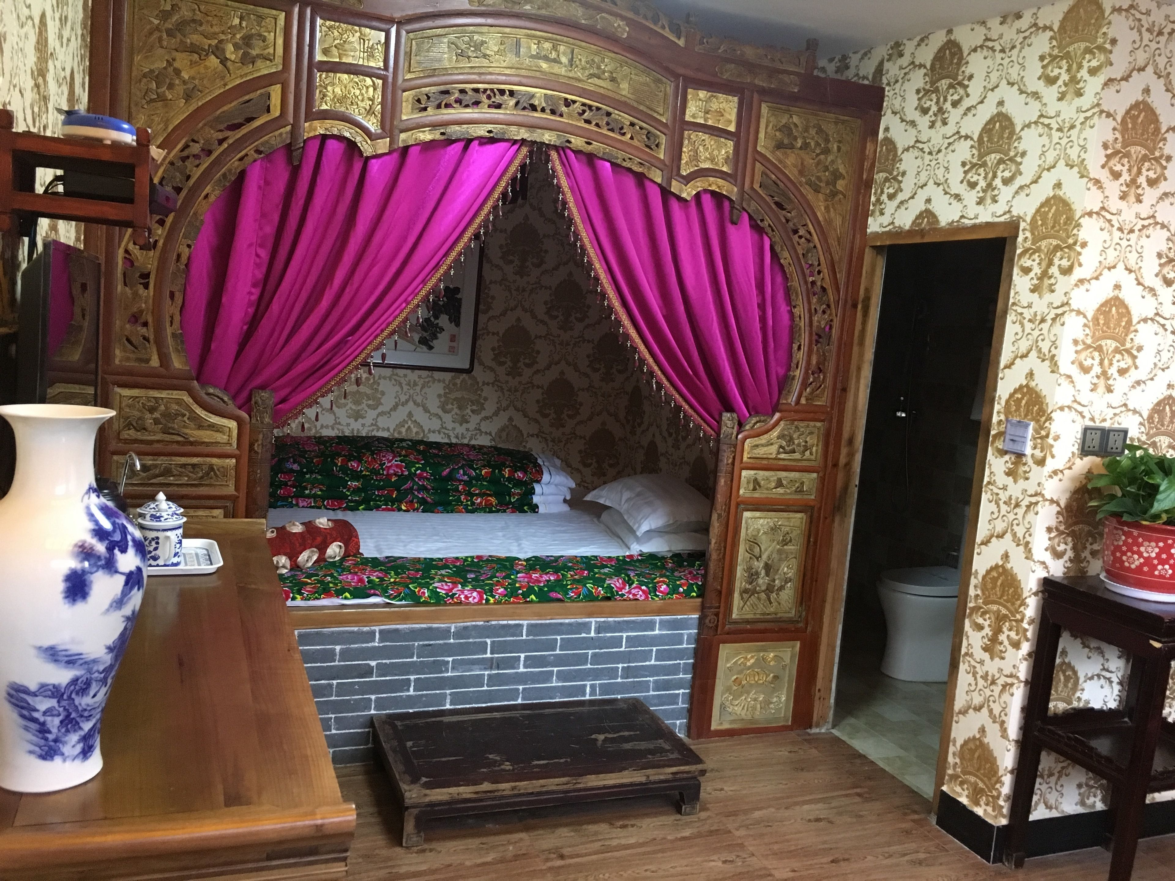 A room with a bed, a wooden bench, a vase, and a potted plant.