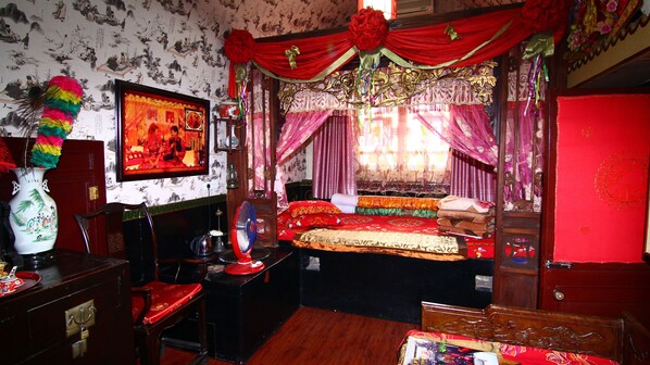 A traditional room with a bed, a desk, a chair, a vase, and a red door.