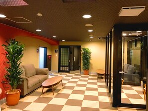 En reception med et ternet gulv, en sofa, et sofabord, en potteplante og en glasdør, der fører til et andet rum.