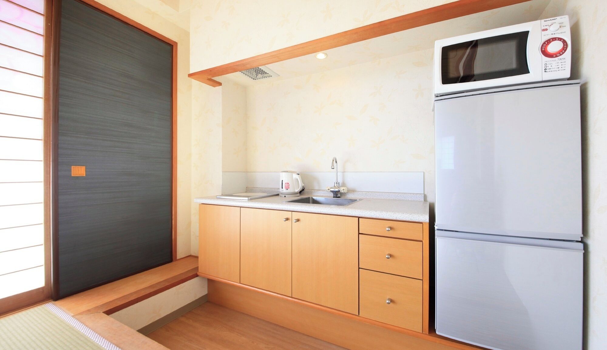 A compact kitchen with a microwave, a refrigerator, a sink, and wooden cabinets.