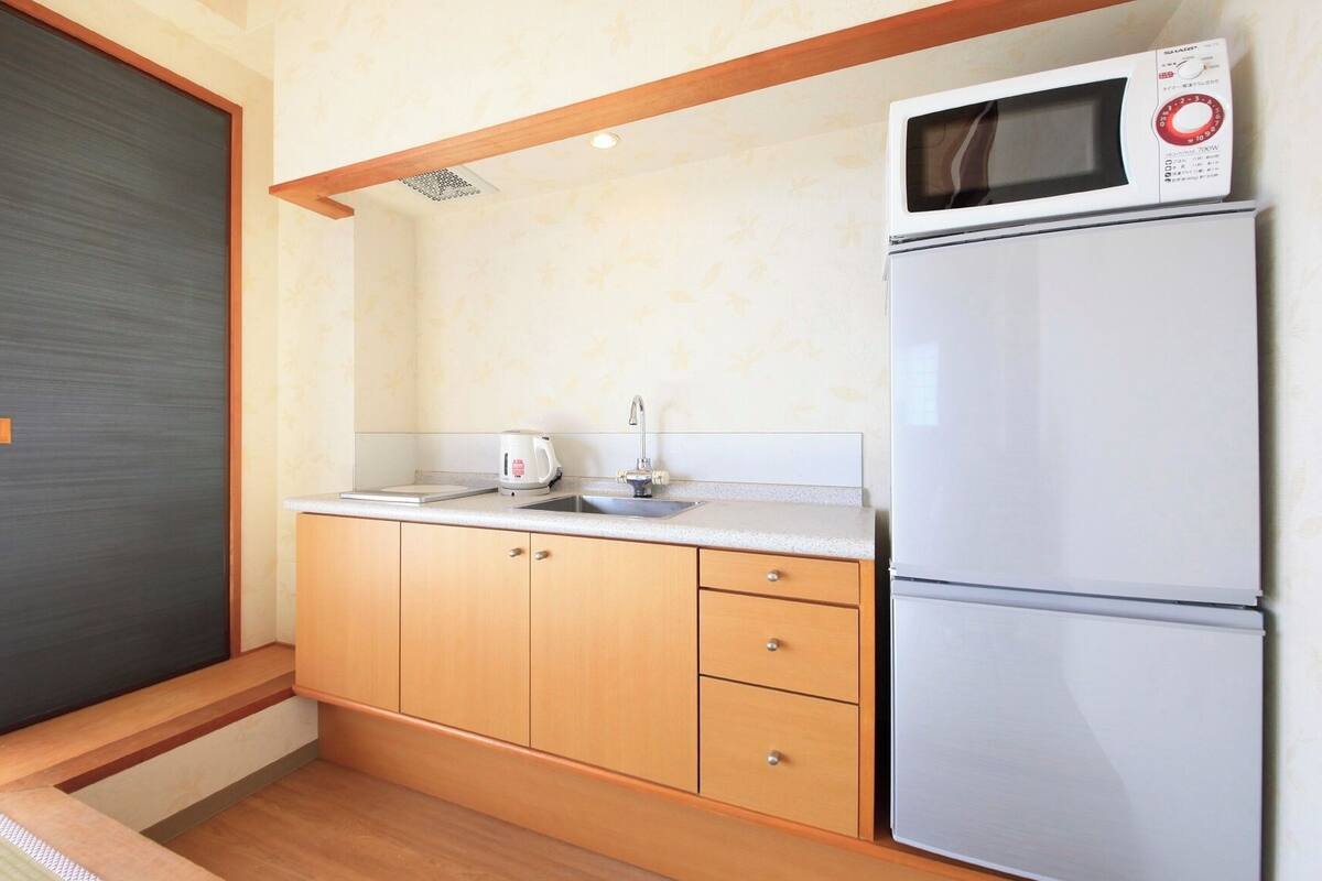 A compact kitchen with a microwave, a refrigerator, a sink, and wooden cabinets.