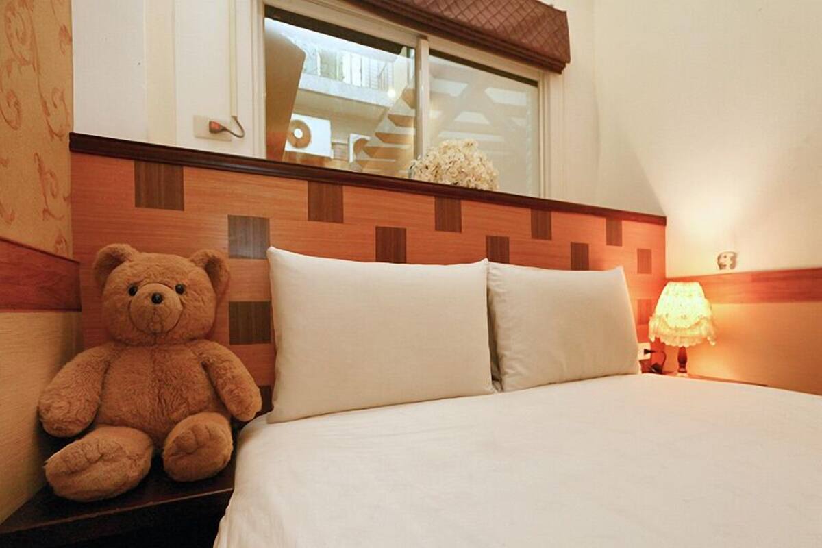 A hotel room with a bed, a nightstand, a lamp, and a teddy bear.
