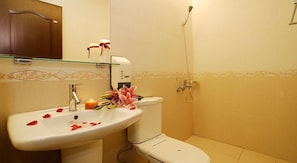 A bathroom with a white sink, toilet, and shower. There is a mirror above the sink and a decorative tile border on the walls.