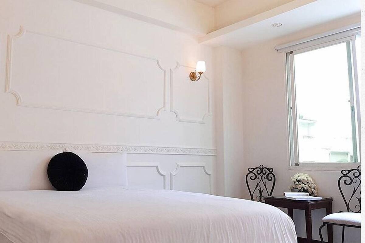 A bedroom with a large bed, a bedside table, a chair, and a window.