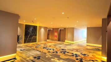 A hotel corridor with a patterned carpet, doors, and recessed lighting.