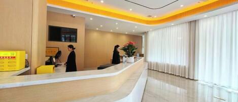 A hotel reception area with a curved reception desk, a flat-screen TV, and a large window with curtains.