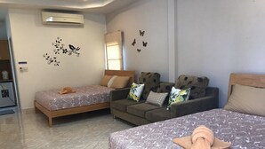 A hotel room with two single beds, a sofa, and a large bed. There is a window with curtains, a wall-mounted air conditioner, and decorative butterfly decals.