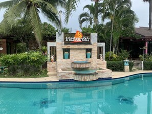 Ein Poolbereich mit einer Steinstruktur, Palmen und einem Schild mit thailändischem Text.