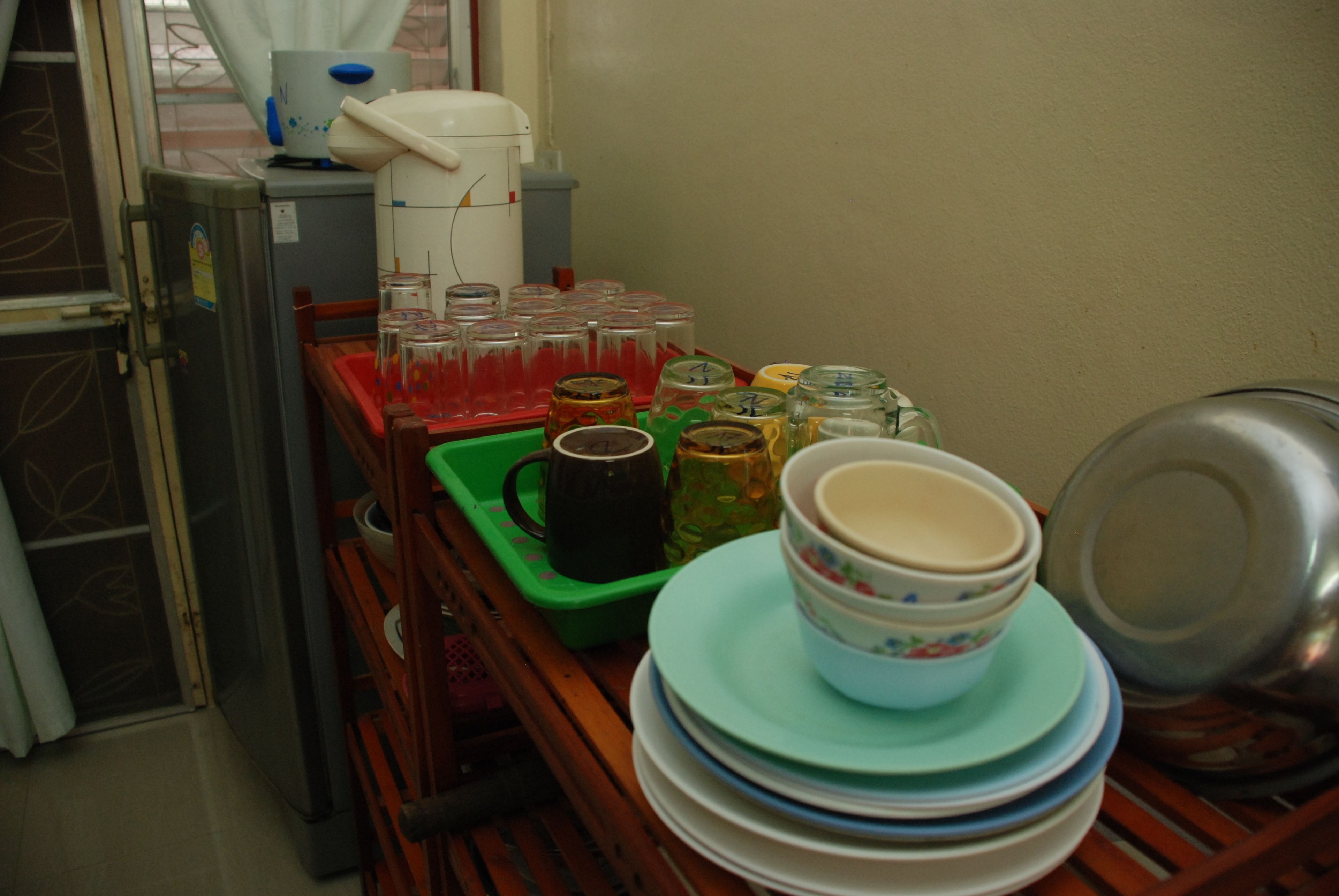 Un coin cuisine équipé d’un réfrigérateur, d’une machine à café, ainsi que de divers plats et récipients rangés sur une étagère en bois.