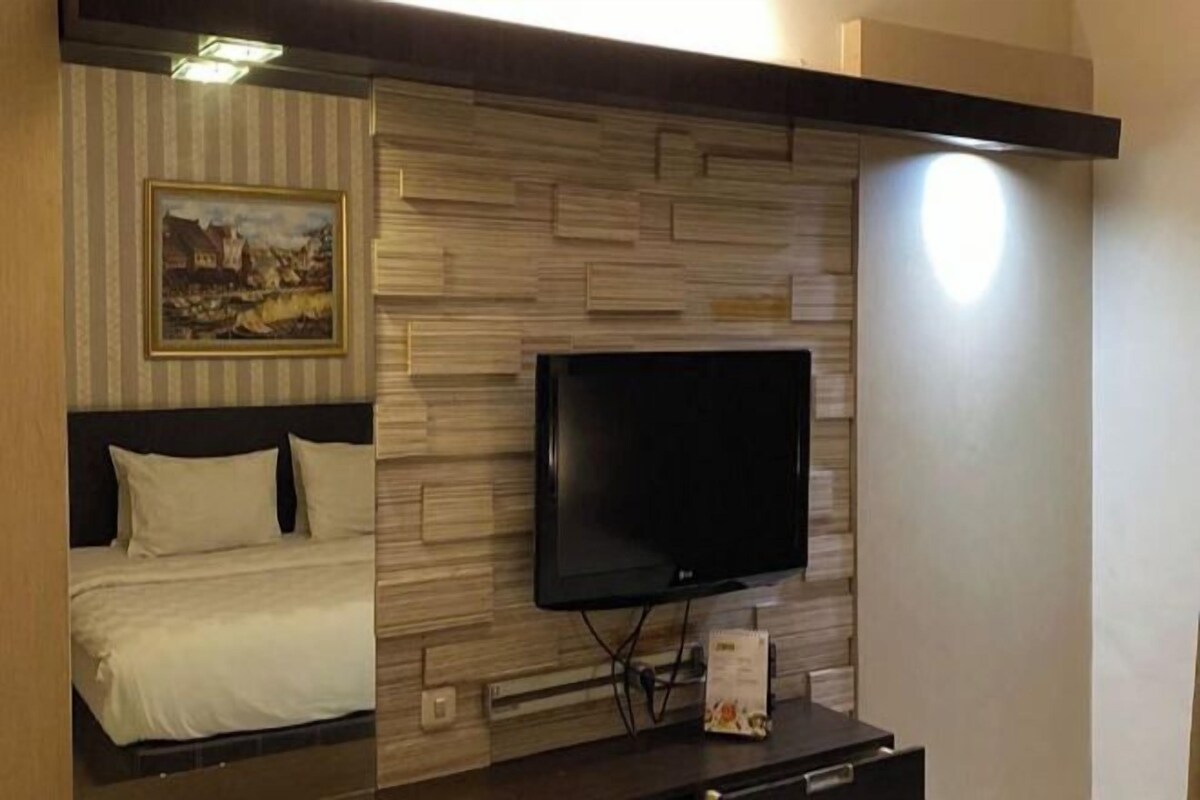 A hotel room with a bed, a flat-screen TV mounted on a wooden wall, and a framed picture above the bed.