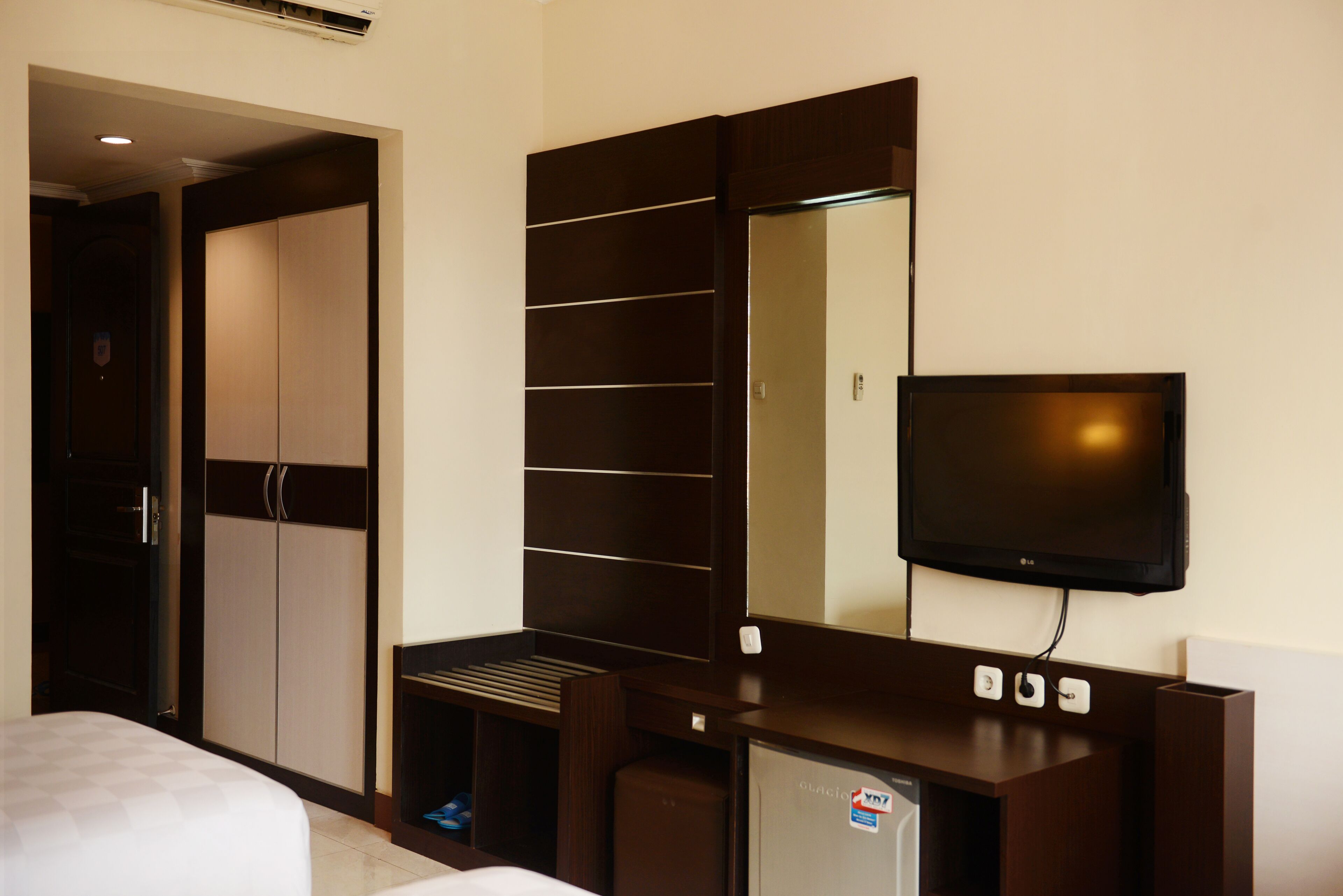 A hotel room with a bed, a wardrobe, a built-in TV, and a mini-fridge.
