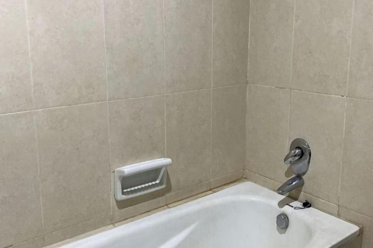 A bathroom with a white bathtub, a handheld showerhead, and a small shelf unit.