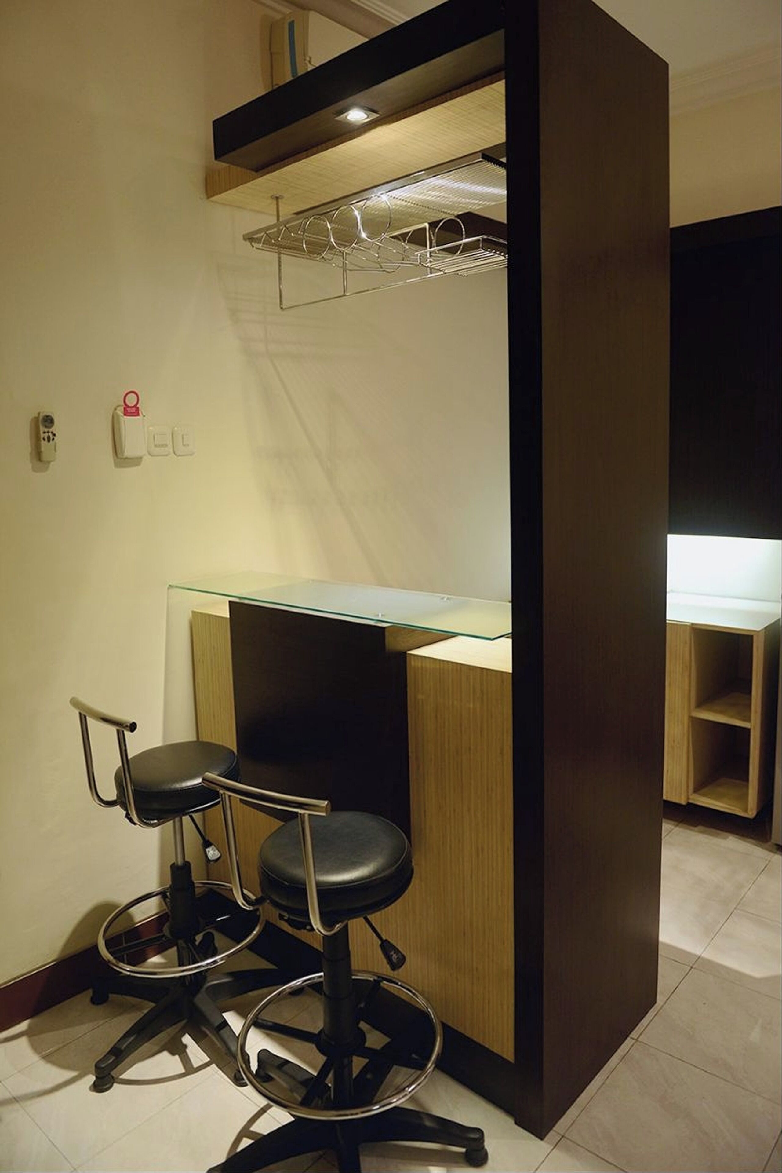 A modern office space with a desk, two black office chairs, a glass partition, and a ceiling-mounted light fixture.