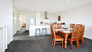 A modern kitchen with white cabinets, a central island, and a dining area with wooden chairs and a table. - Bayside (Aldinga Beach)