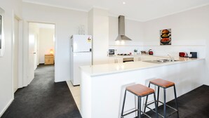 A modern kitchen with a central island, bar stools, a built-in oven, and a stainless steel sink. - Bayside (Aldinga Beach)