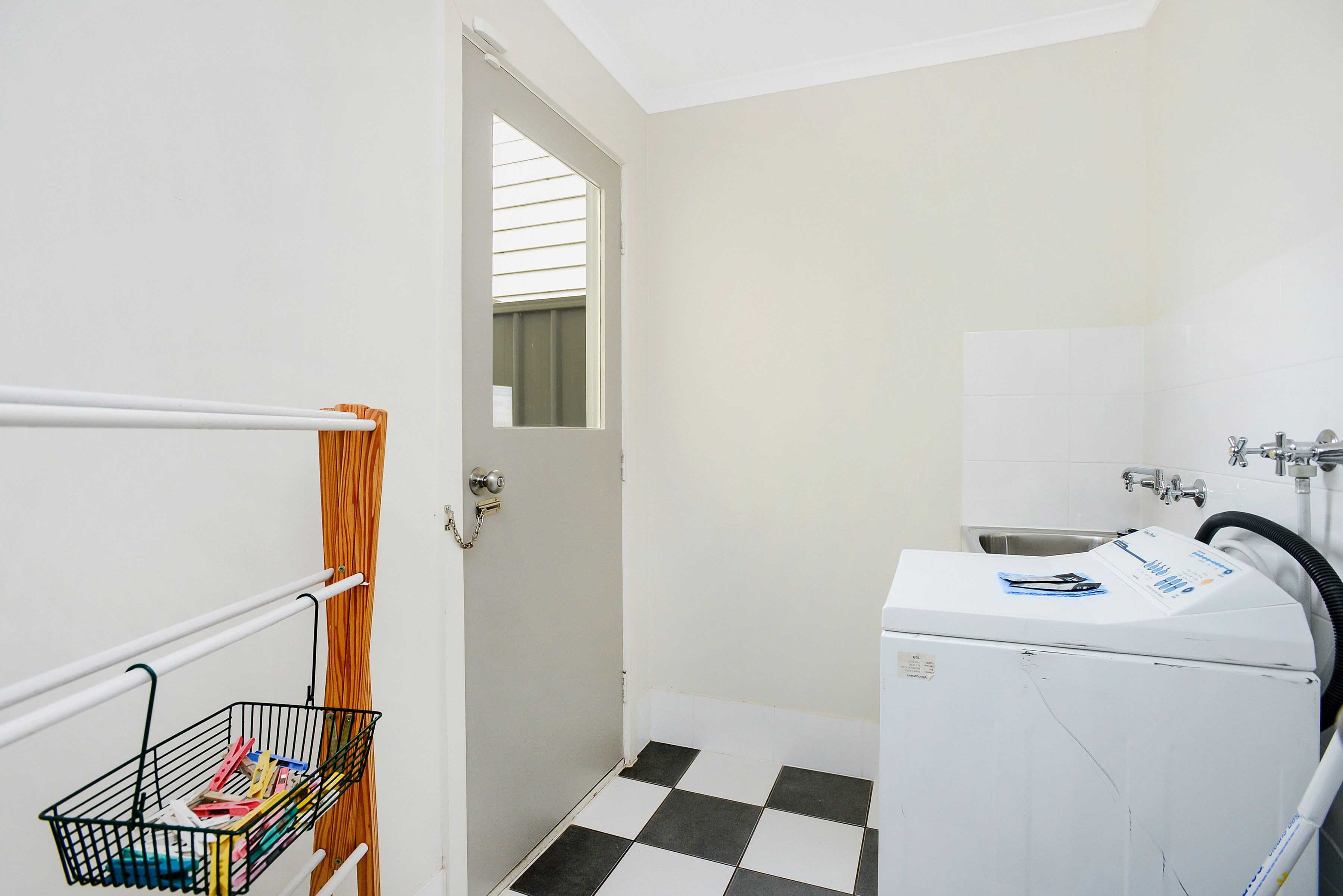 A laundry room with a washing machine, a sink, and a metal rack with a basket.