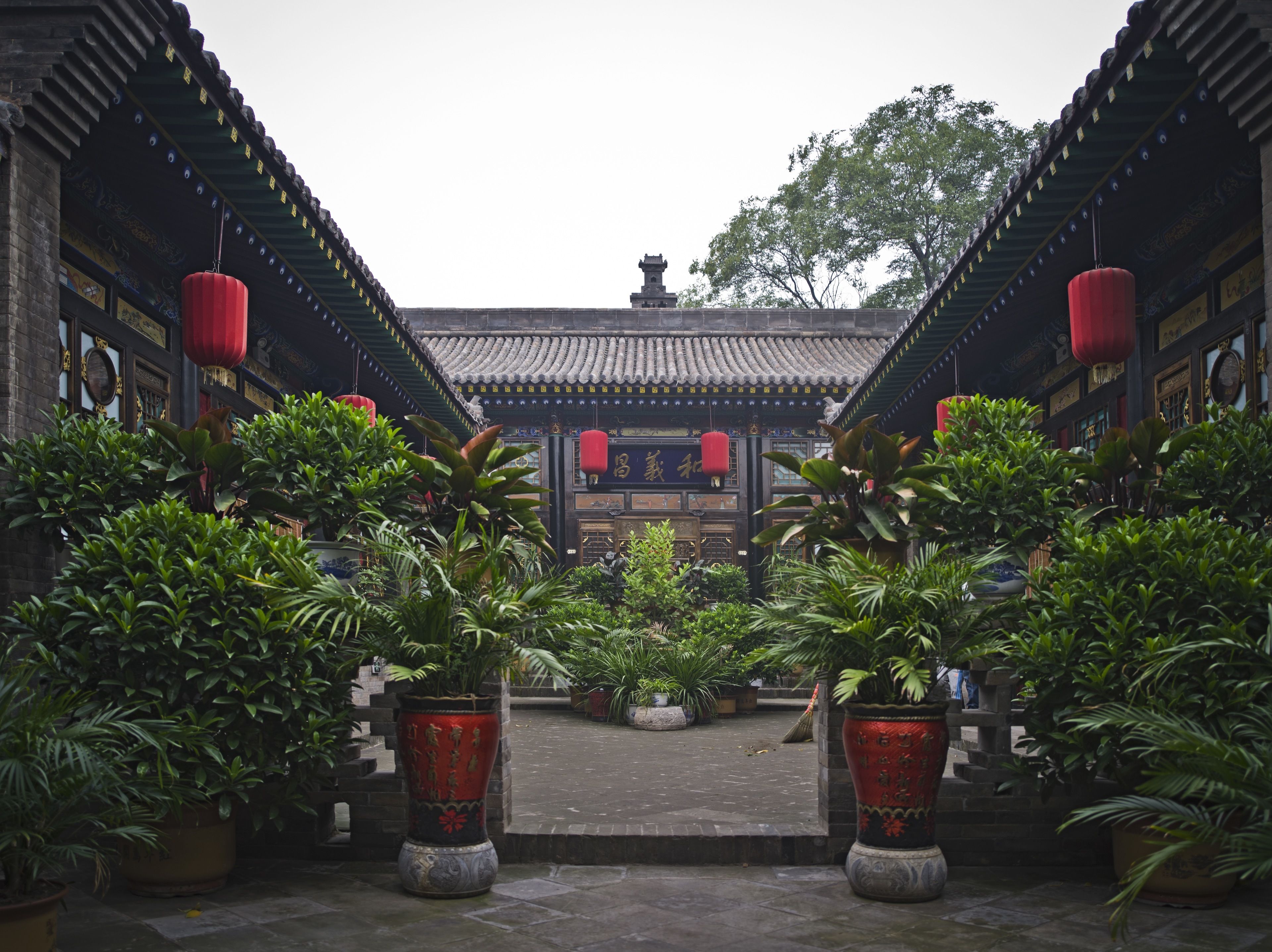 A traditional courtyard with tiled roofs, potted plants, and red lanterns.