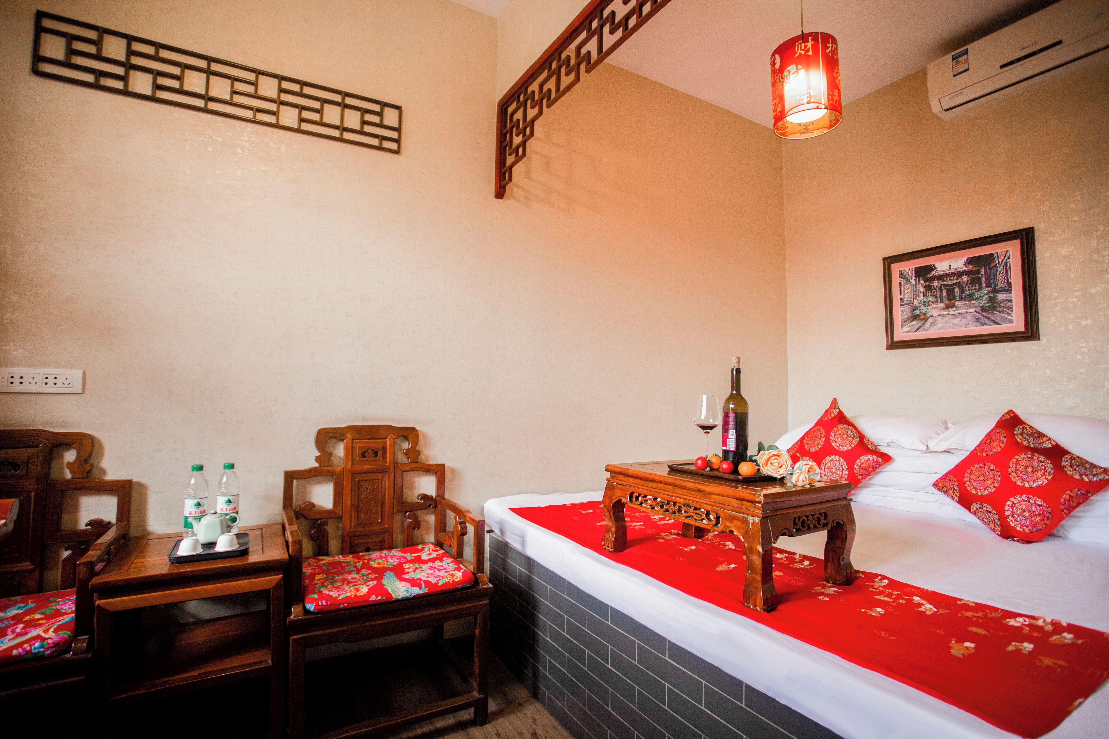 A hotel room with a bed, a wooden nightstand, a chair, a table, and a wall-mounted air conditioner.