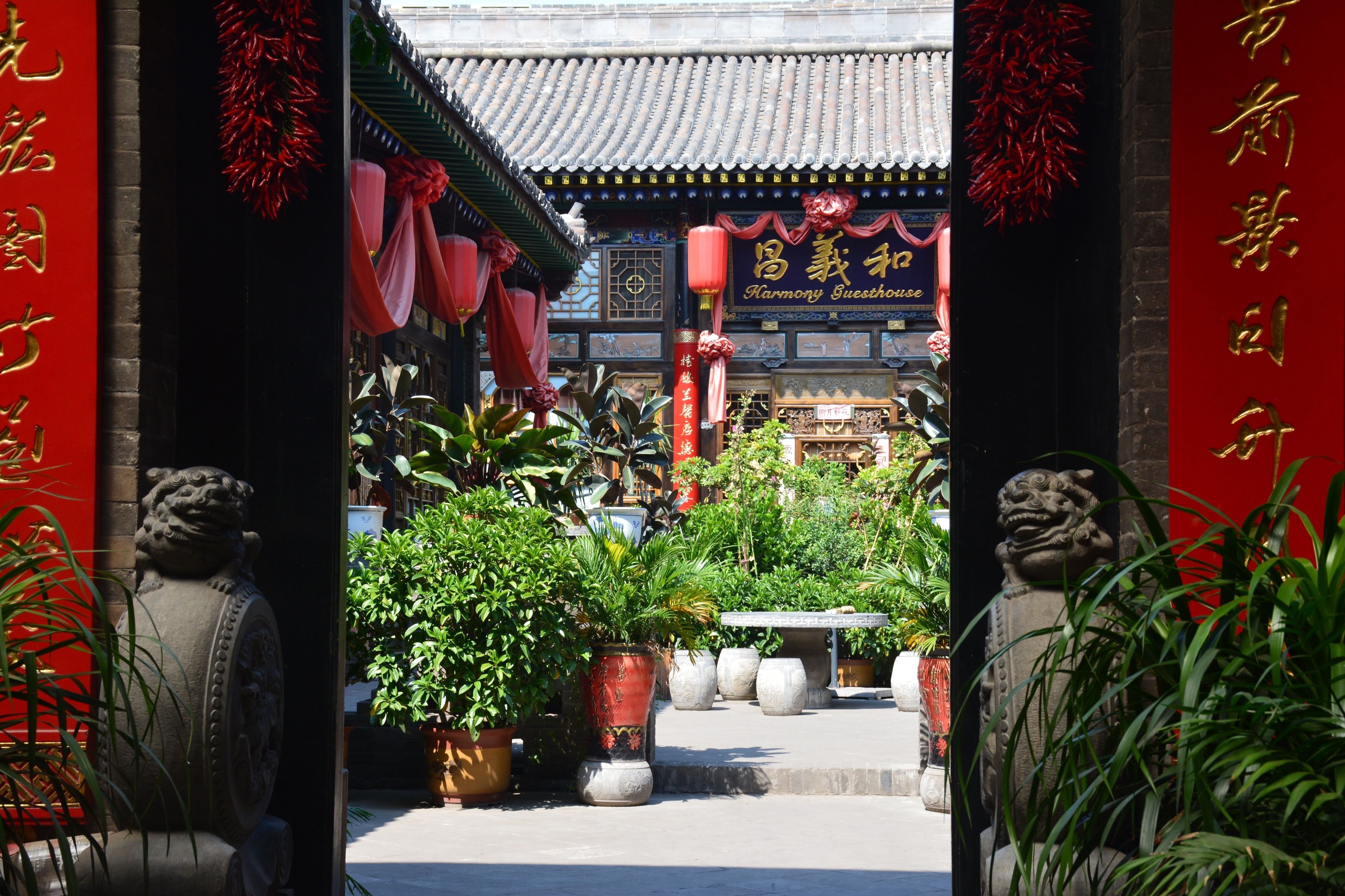 A traditional Chinese gate with red decorations and a Harmony Guesthouse sign.
