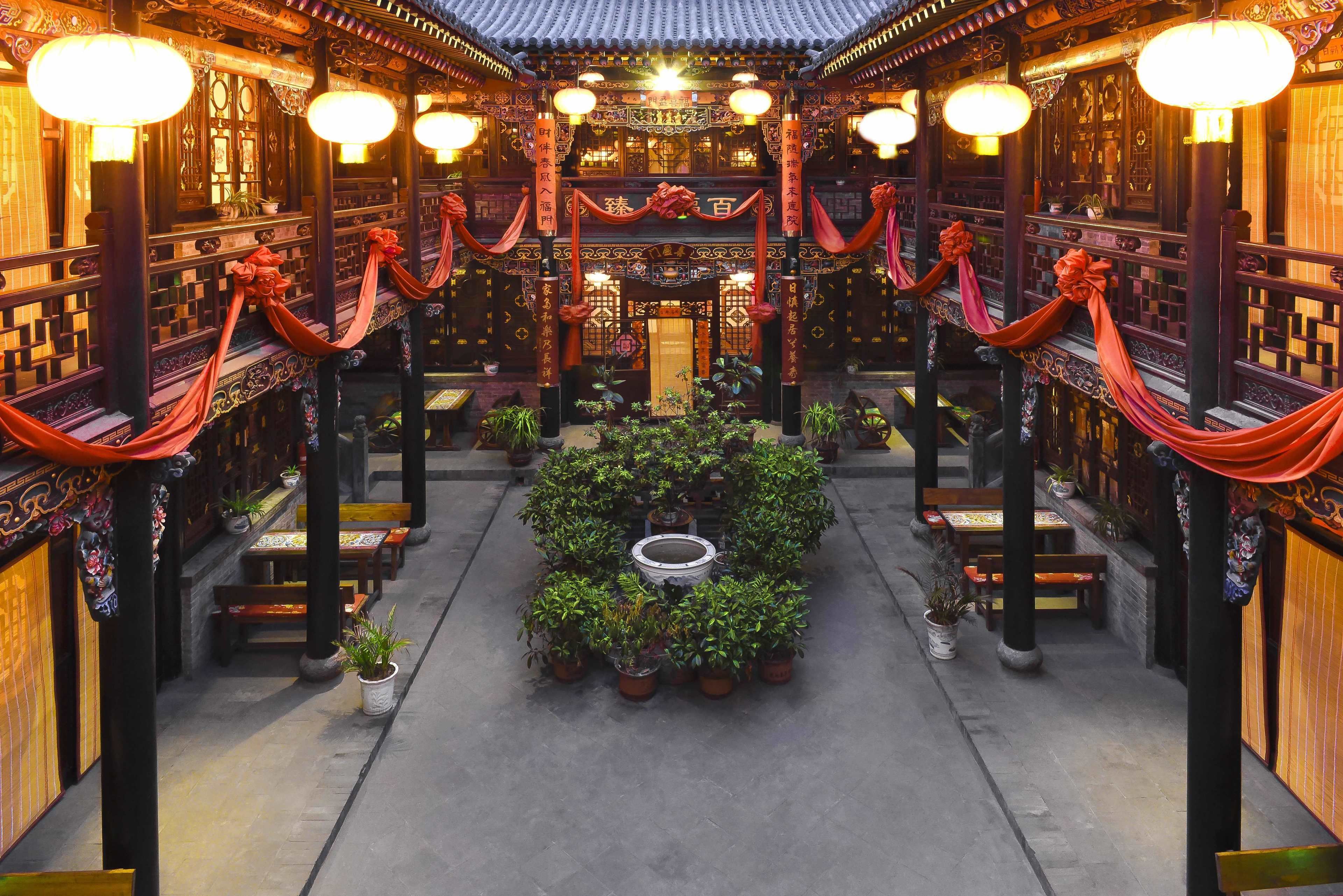 A traditional courtyard with wooden architecture, lanterns, and potted plants.