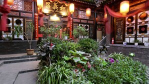 Un edificio tradicional chino con puertas de madera ornamentadas y un jardín cuidado con diversas plantas en macetas.