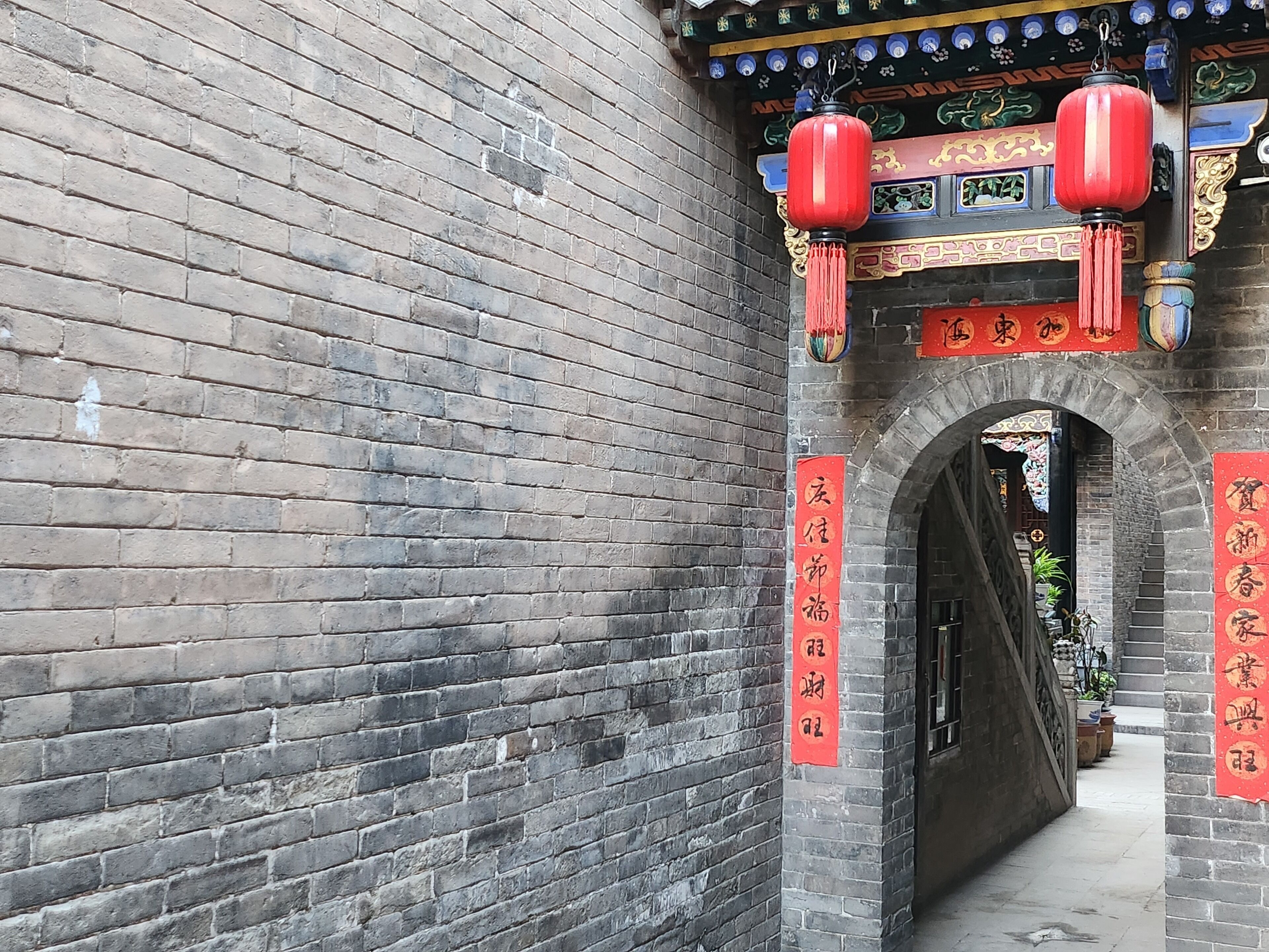 A traditional brick wall with an arched entrance, red lanterns, and Chinese characters on banners.