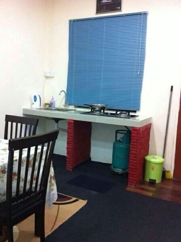 A small kitchenette with a gas stove, a sink, and a window with blinds. There is a chair and a table with a floral tablecloth.