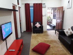 A living room with a TV, two sofas, a red cushion, and a red bench.