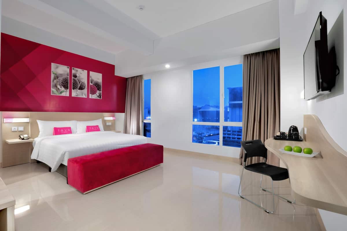 A modern hotel room with a large bed, a desk with a chair, a TV, and a window with a city view.