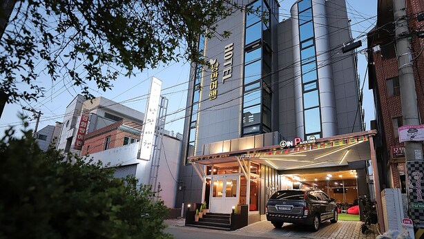 Ein Hotel mit moderner Fassade, einem Parkplatzschild und einem davor stehenden Auto.