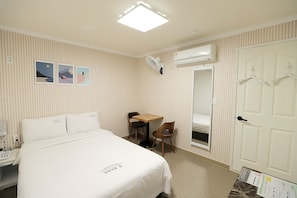 Relax in a clean and simple room with a comfortable bed, a small table for two, and a large mirror.