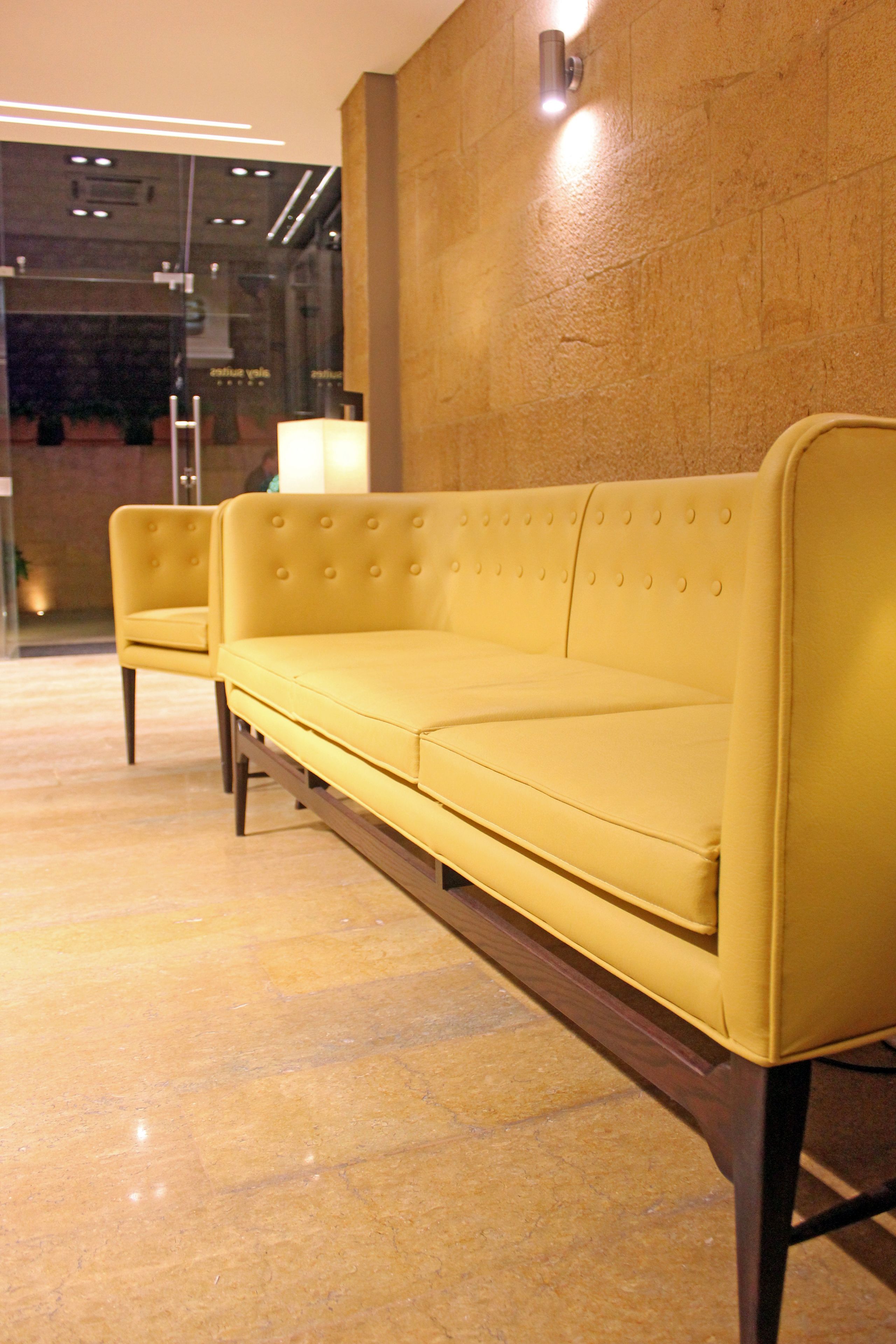 A yellow sofa and armchair in a lobby with a marble floor and a textured wall.