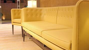 A yellow sofa and armchair in a lobby with a marble floor and a textured wall.