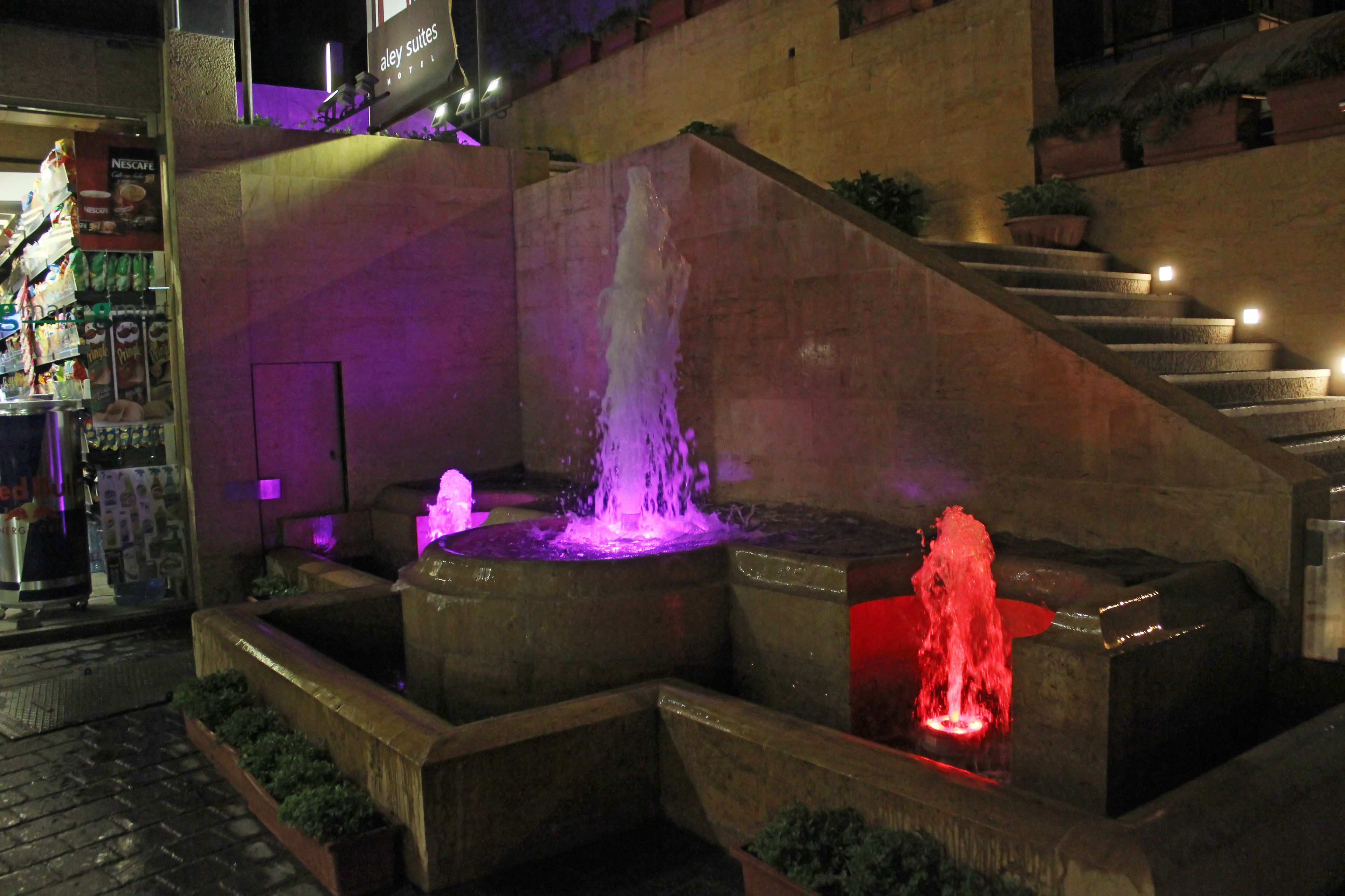 A nighttime outdoor area with a fountain, steps, and a Nescafe display.