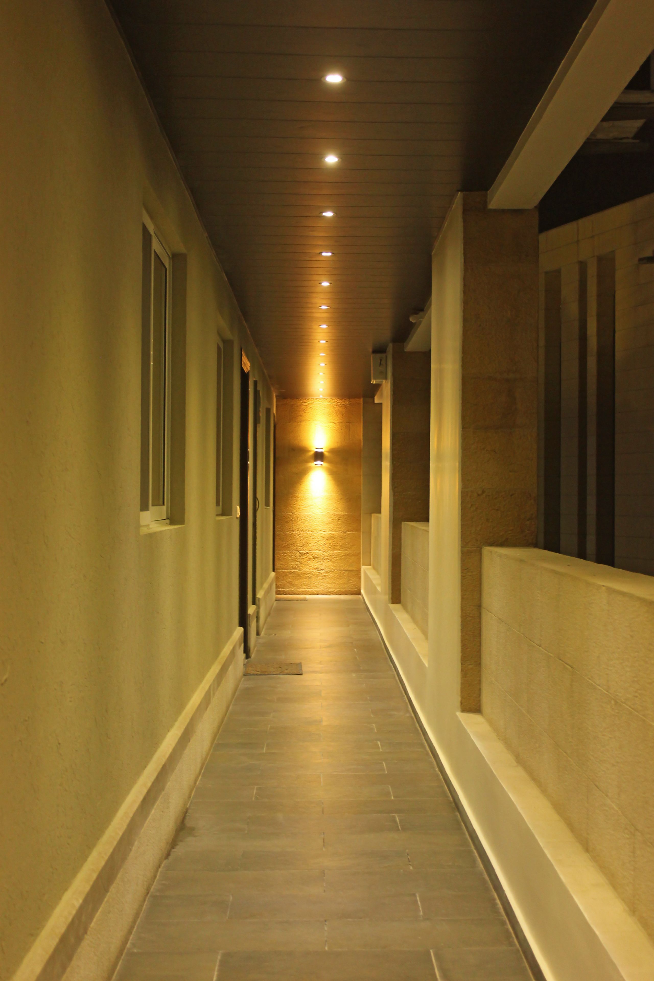 A corridor with a wooden ceiling, recessed lighting, and a wall-mounted light fixture.