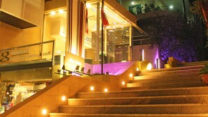 A staircase leading to a brightly lit building with a glass facade and a sign indicating a bakery and stuff. - Aley Suites (Aley)