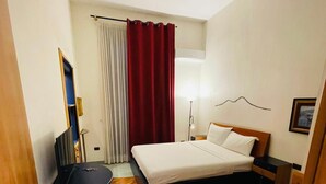 A compact hotel room with a bed, a desk, a chair, and a lamp. - Santa Maria La Nova 21 B&B (Naples)