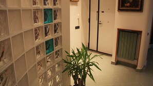 A hallway with a plant, a door, and a wall with framed pictures. - Santa Maria La Nova 21 B&B (Naples)