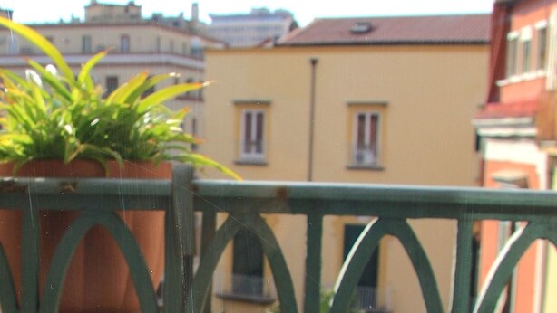 A balcony with a view of a narrow street, buildings, and a yellow car parked on the side. - Santa Maria La Nova 21 B&B (Naples)
