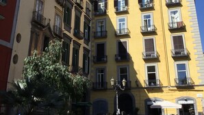 A yellow building with multiple balconies and windows, a street in front, and a tree to the left. - Santa Maria La Nova 21 B&B (Naples)