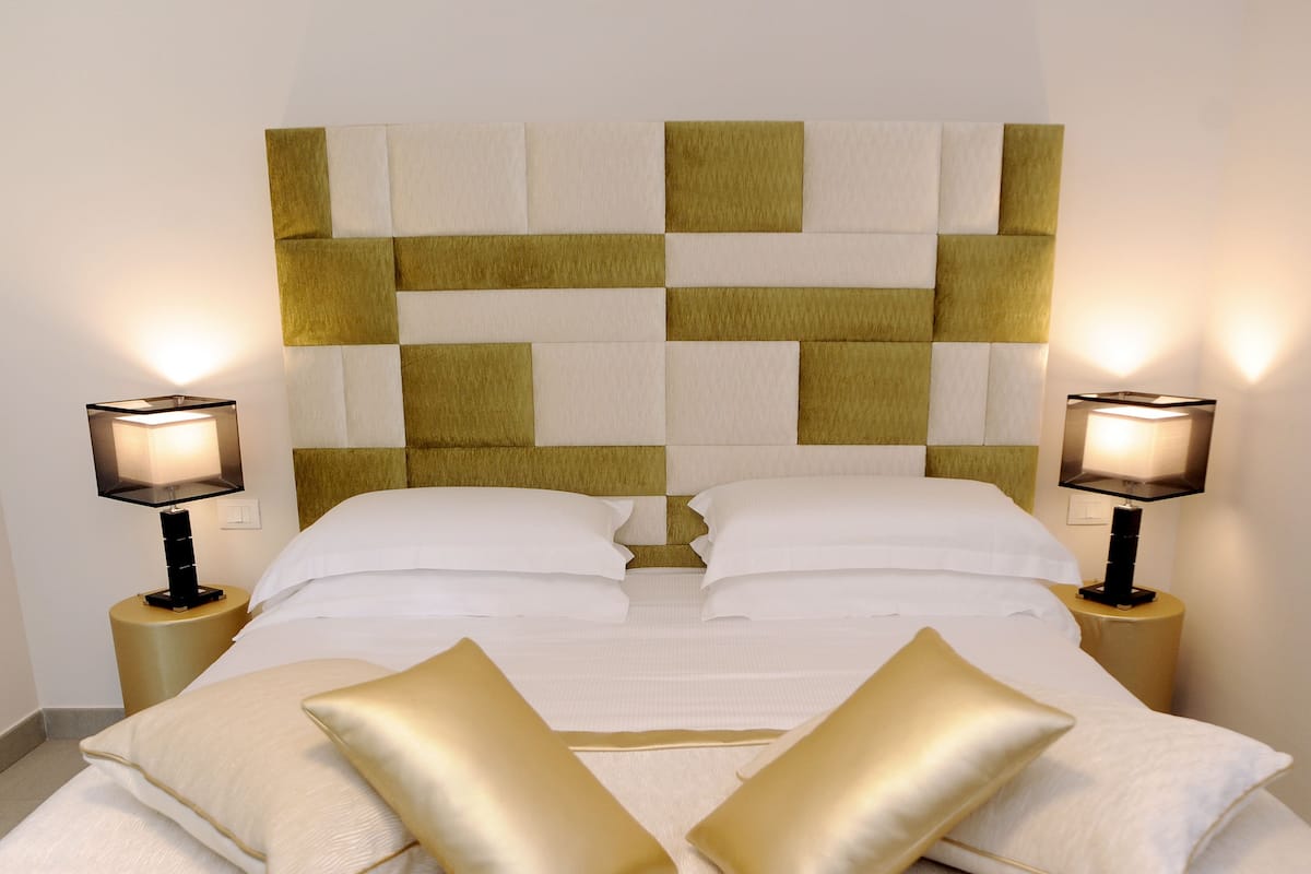A neatly made bed with white and gold pillows, a checkered headboard, and two bedside lamps on matching nightstands.