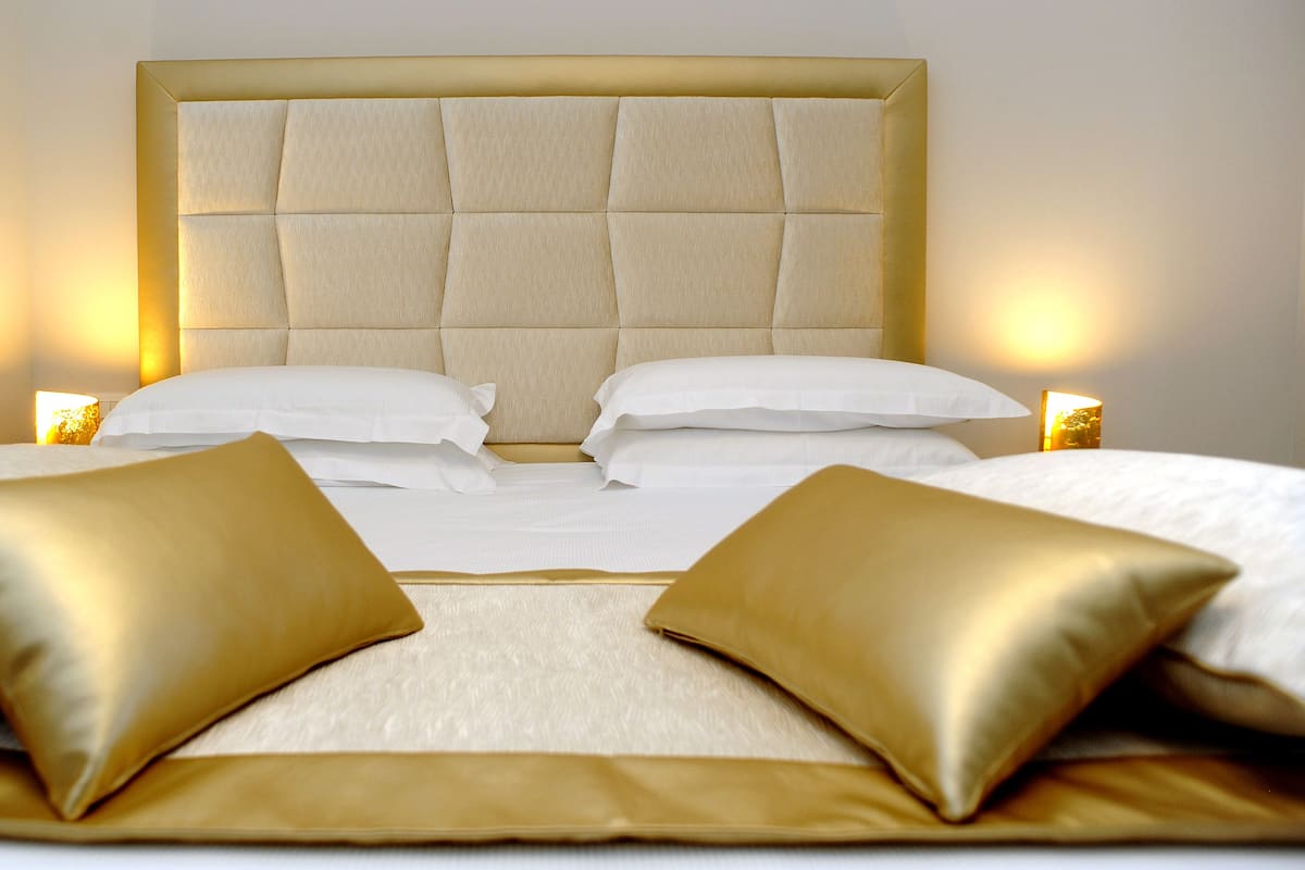 A neatly made bed with a tufted headboard, two gold pillows, and two bedside lamps.