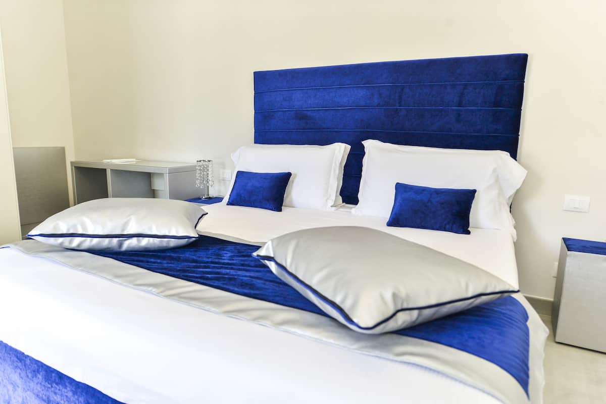 A neatly made bed with a blue headboard, white and blue bedding, and two bedside tables with lamps.