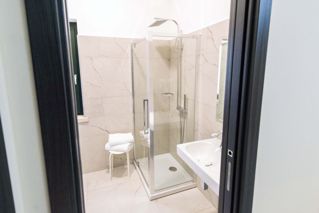 Un baño moderno con cabina de ducha de vidrio, un lavabo blanco y un taburete blanco pequeño.